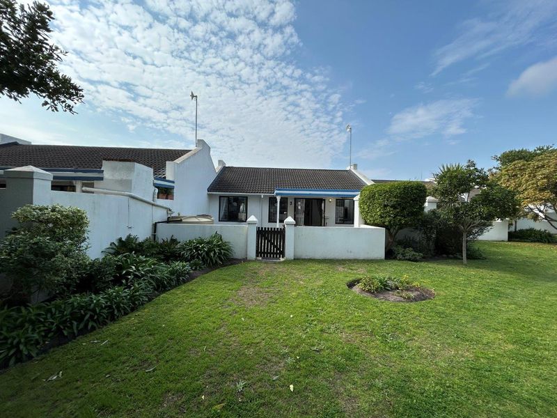 Front view of a townhouse featuring a private garden, boundary wall with pedestrian gate, and a tiled roof structure.