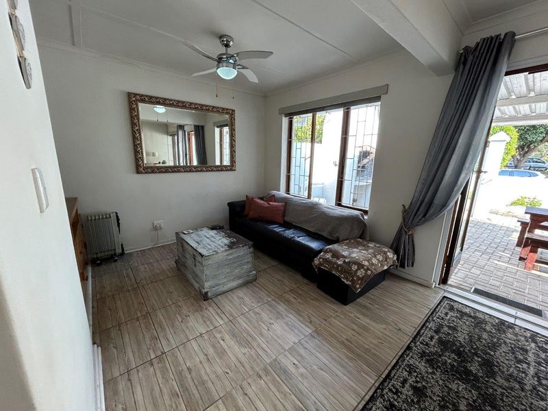 A living room featuring tiled flooring, a ceiling fan, and large windows with security bars, providing direct access to an outdoor patio area.