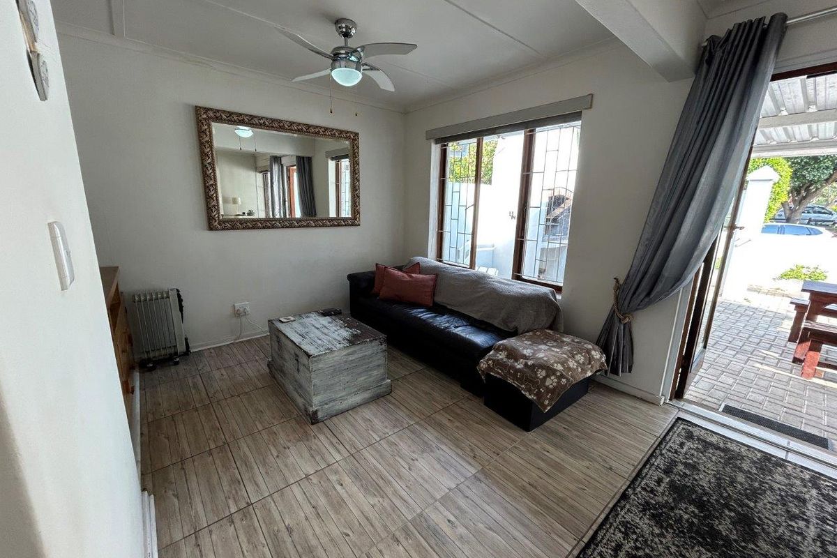 A living room featuring tiled flooring, a ceiling fan, and large windows with security bars, providing direct access to an outdoor patio area.