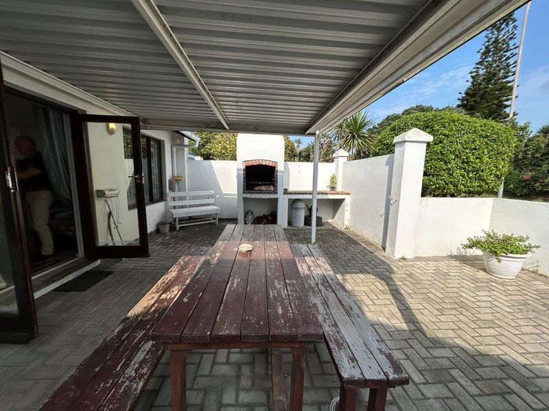 A covered outdoor patio area featuring a built-in braai, paved flooring, and direct access to the interior living space.