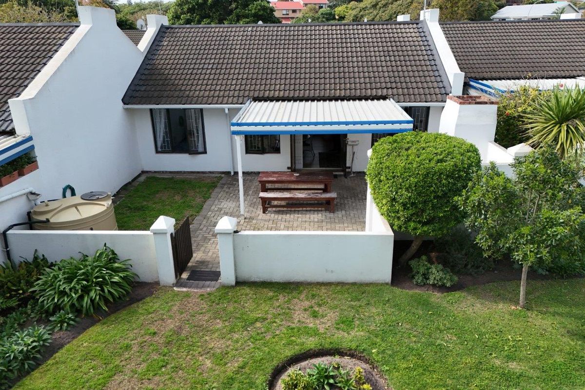 Aerial view of the rear exterior featuring a paved patio area, covered veranda, water tank, and private garden space.
