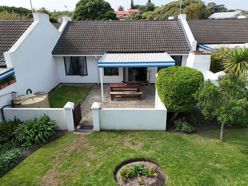 Aerial view of the rear exterior featuring a paved patio area, covered veranda, water tank, and private garden space.