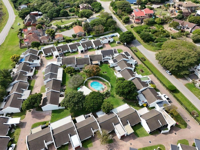 Aerial view of a townhouse complex featuring multiple residential units, a central communal swimming pool, landscaped gardens, and paved access roads.