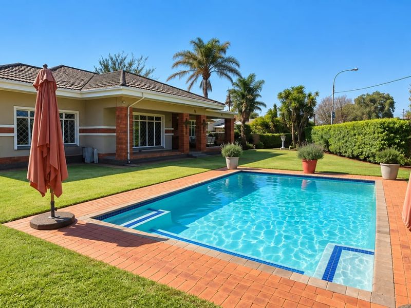 A well-maintained rear garden featuring a clear swimming pool with brick paving, set against a single-story home with a covered patio area.