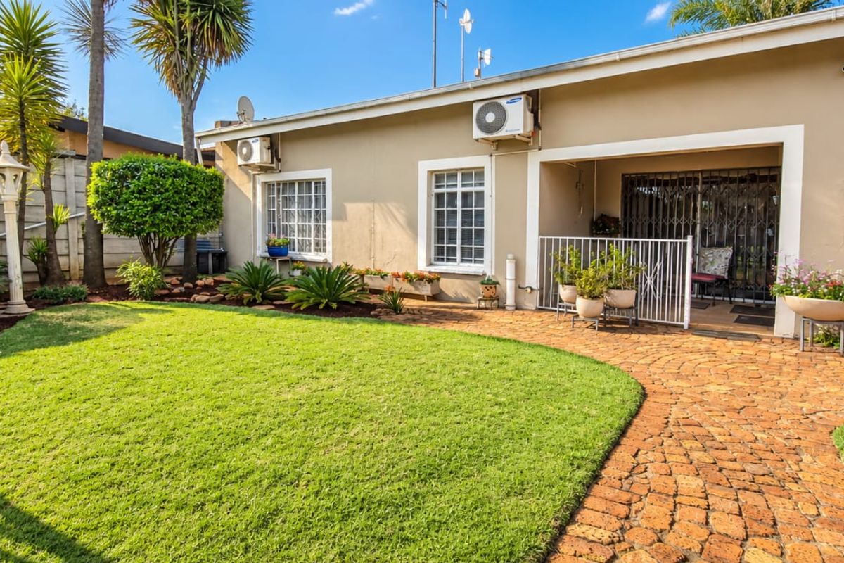 A well-maintained rear garden featuring a brick-paved patio area, manicured lawn, and secure access to the home's exterior.