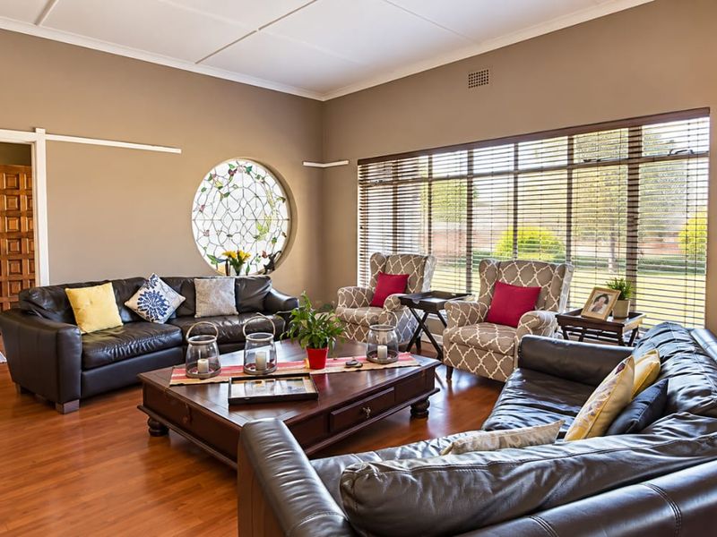 Spacious living room featuring warm laminate flooring, a unique circular feature window, and large windows with venetian blinds allowing for ample natural light.