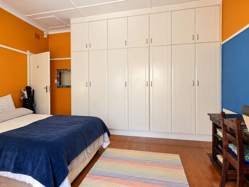 A bedroom featuring extensive floor-to-ceiling built-in cupboards, hardwood flooring, and a classic picture rail, offering ample storage space.