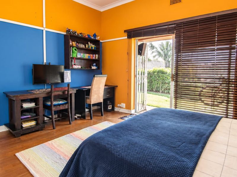 Spacious bedroom featuring hardwood flooring, built-in wardrobes, and direct access to the garden through a sliding glass door with security gate.