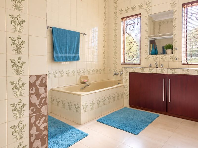 A dated bathroom featuring a built-in bathtub, vanity cabinetry, and decorative tiled walls with natural light from two windows.