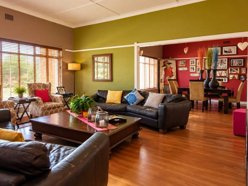 Spacious open-plan living and dining area featuring polished hardwood flooring, large windows with venetian blinds, and a bright, multi-colored interior design.
