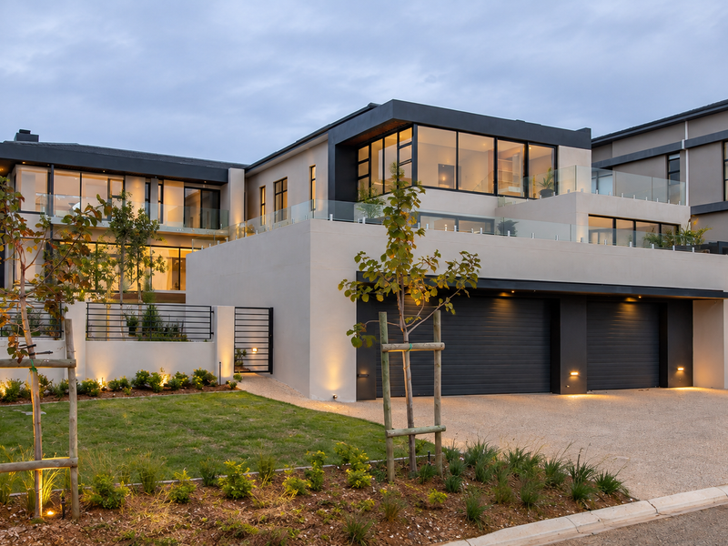 Modern luxury residence featuring a double garage, expansive glass balustrades, and professionally landscaped front garden with integrated exterior lighting.