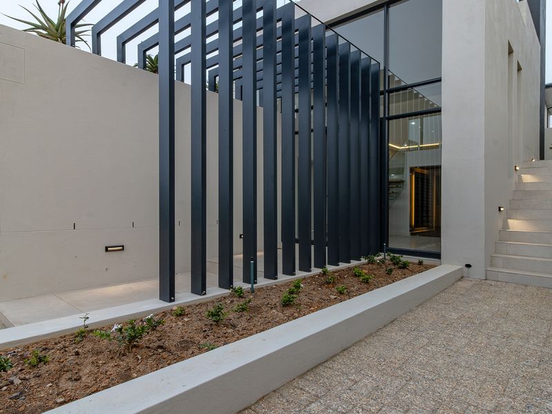 Modern architectural front entrance featuring a striking metal pergola, stone staircase, and clean concrete finishes with integrated lighting.