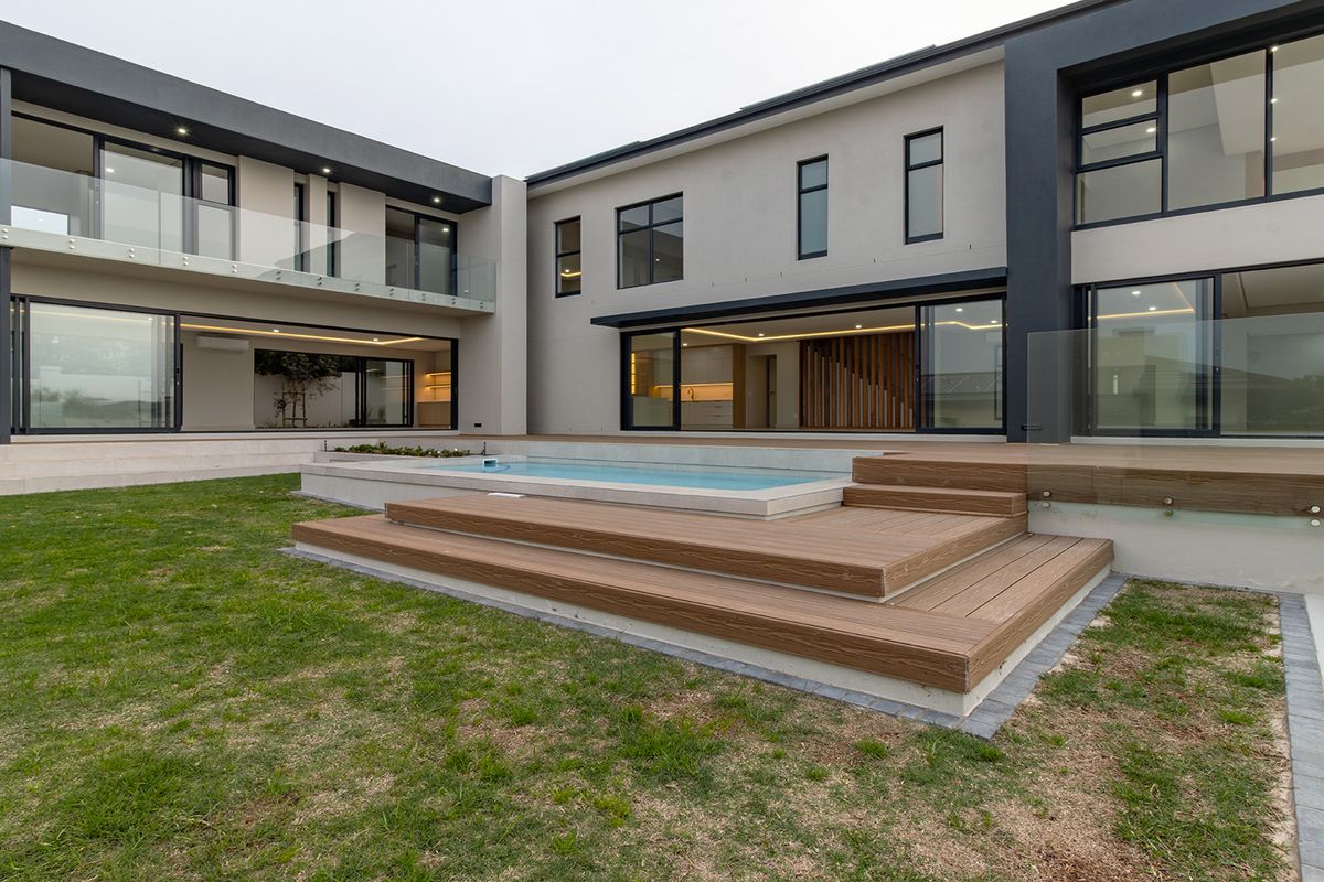 Modern rear exterior featuring a swimming pool, timber decking, glass balustrades, and expansive sliding doors connecting the indoor and outdoor living spaces.
