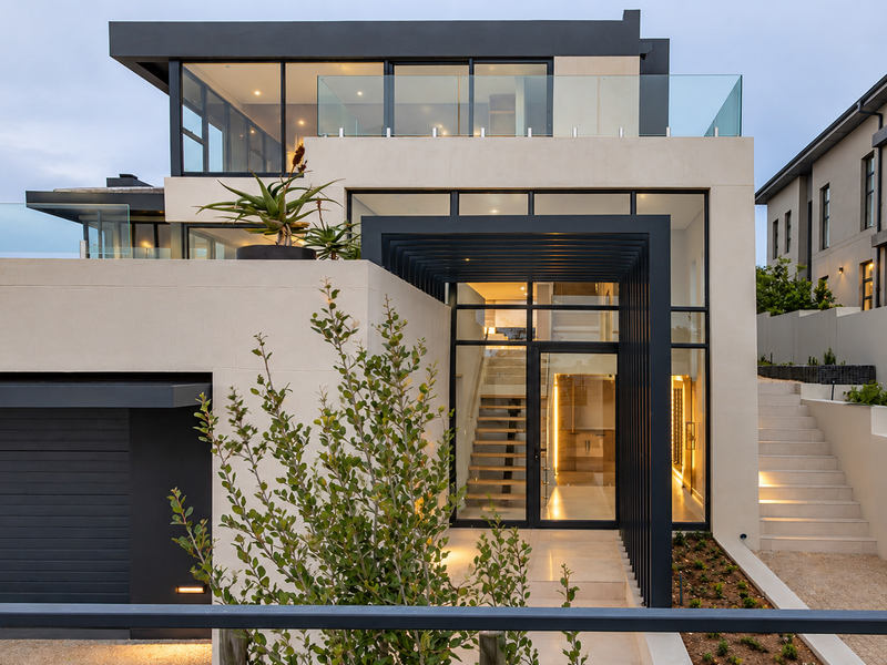 Modern multi-level architectural home featuring a striking glass-fronted entrance, integrated garage, and clean contemporary lines with high-end finishes.