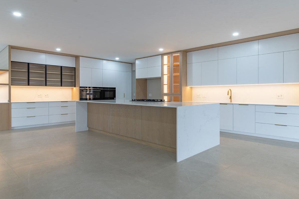 A modern, high-end kitchen featuring sleek white cabinetry, a large central island with quartz countertops, integrated appliances, and warm under-cabinet lighting.