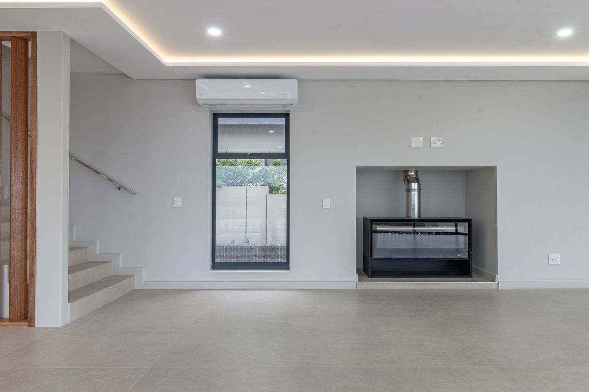A modern, minimalist living area featuring a built-in fireplace, split-system air conditioning, tiled floors, and a stylish timber-slatted staircase.