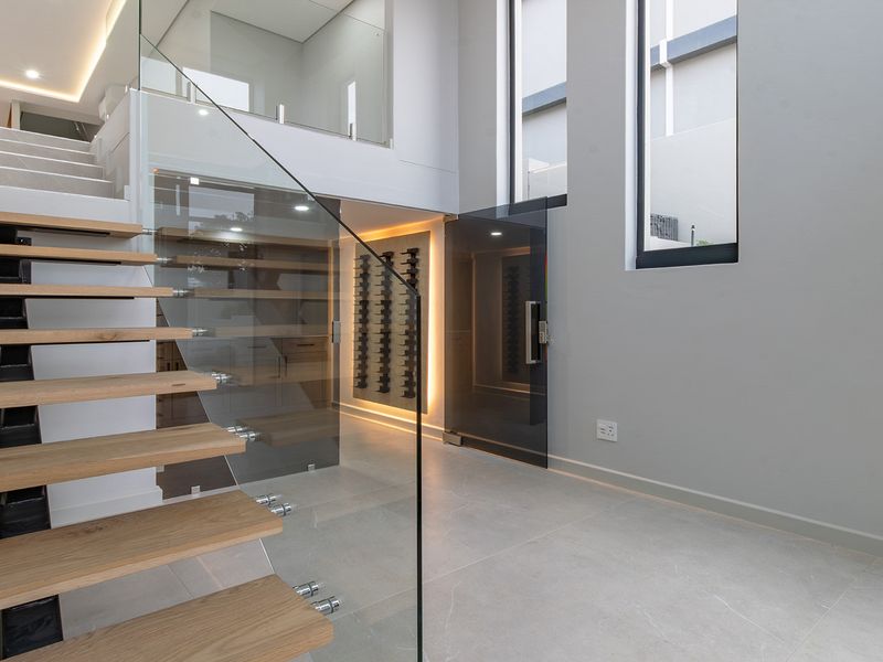 Modern entrance hall featuring a floating timber staircase with glass balustrade, integrated wine cellar, and high-quality porcelain flooring with recessed lighting.
