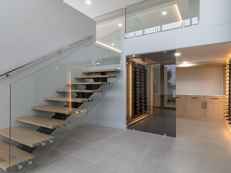 Modern wine cellar featuring custom built-in racking, glass enclosure, and elegant floating staircase with glass balustrade in a contemporary open-plan setting.