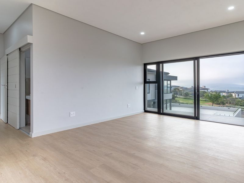 Spacious, modern bedroom featuring light laminate flooring, recessed lighting, and large sliding glass doors opening to an outdoor view.