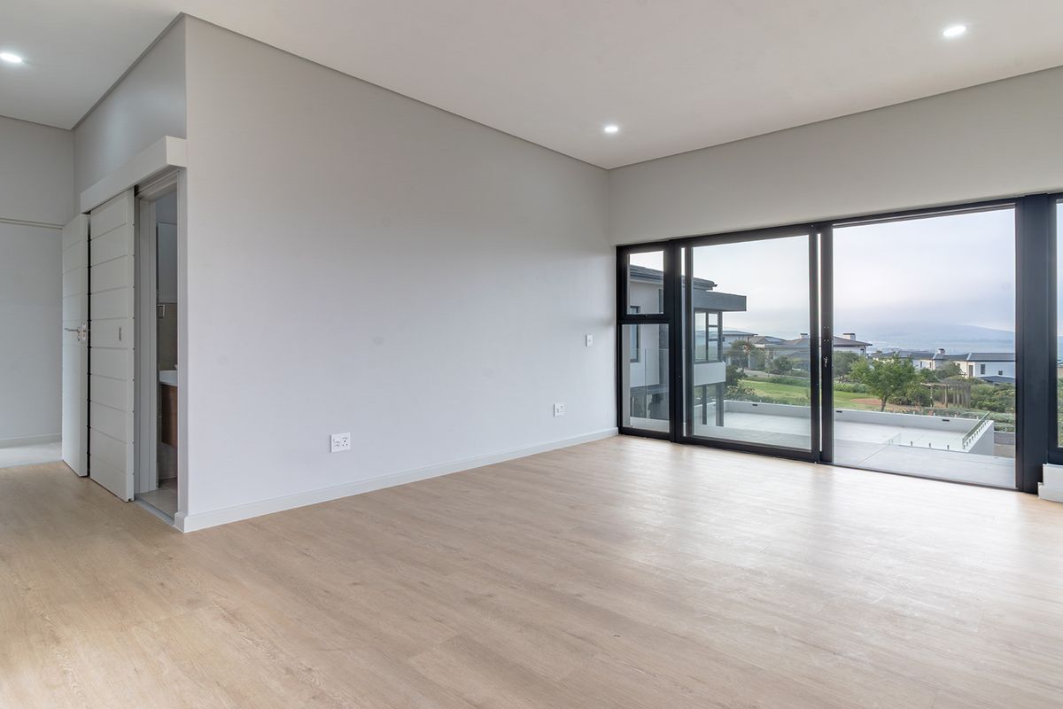 Spacious, modern bedroom featuring light laminate flooring, recessed lighting, and large sliding glass doors opening to an outdoor view.