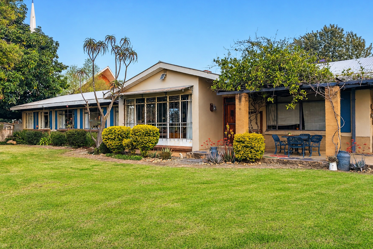 A view of the rear exterior of the house featuring a spacious lawn, a covered patio area, and established garden landscaping.