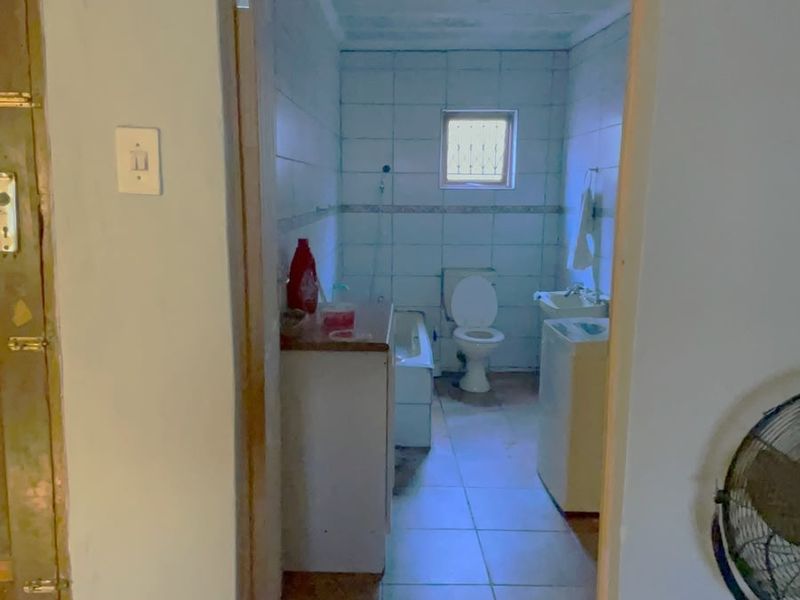 A functional bathroom featuring tiled walls and floors, a standard bathtub, toilet, and washbasin, requiring cosmetic updates to modernize the space.