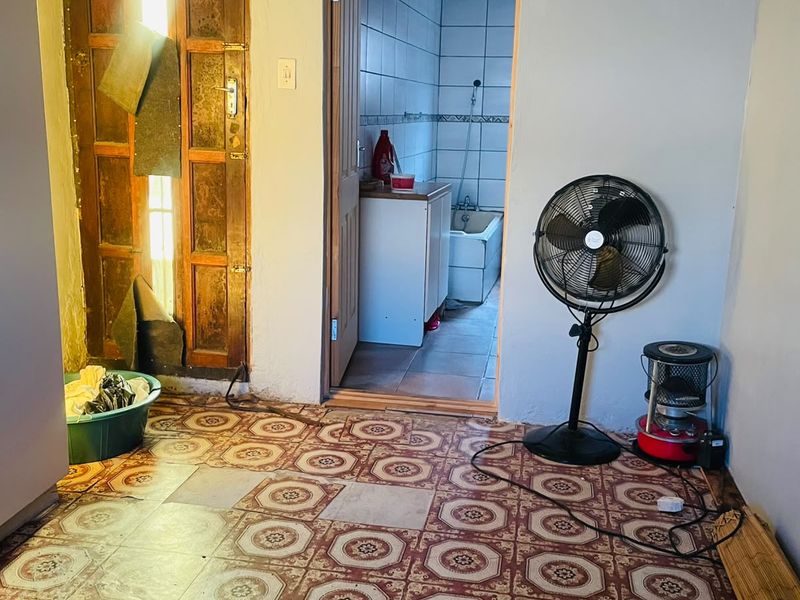 A bedroom space featuring worn patterned floor tiles and a timber door, with an adjacent bathroom visible through the doorway.