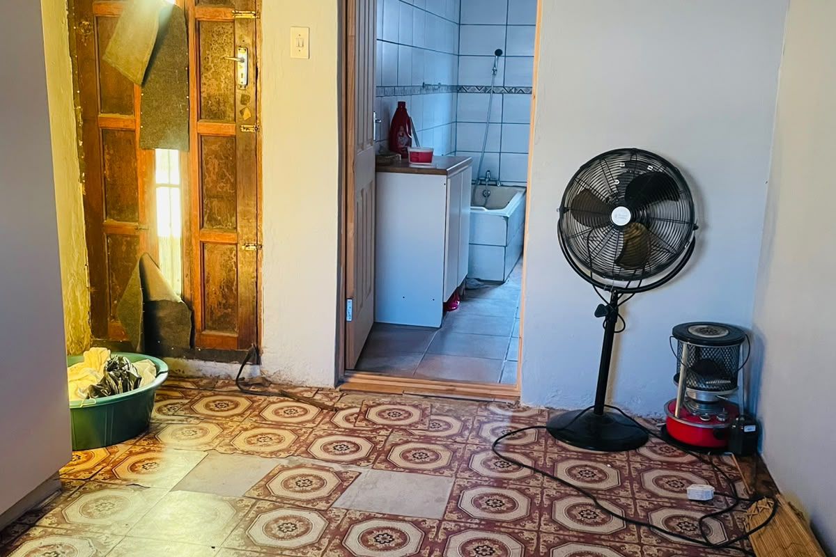 A bedroom space featuring worn patterned floor tiles and a timber door, with an adjacent bathroom visible through the doorway.