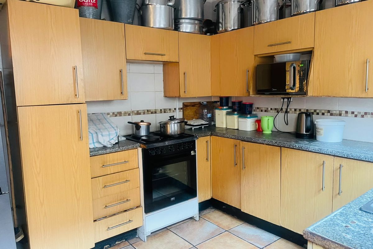 A functional kitchen featuring laminate cabinetry, granite countertops, and a freestanding oven, with tiled flooring and backsplash throughout.
