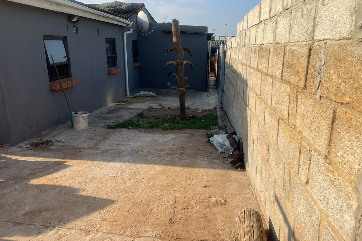 A rear exterior area featuring a concrete boundary wall and paved surface, offering potential for landscaping or outdoor improvement.