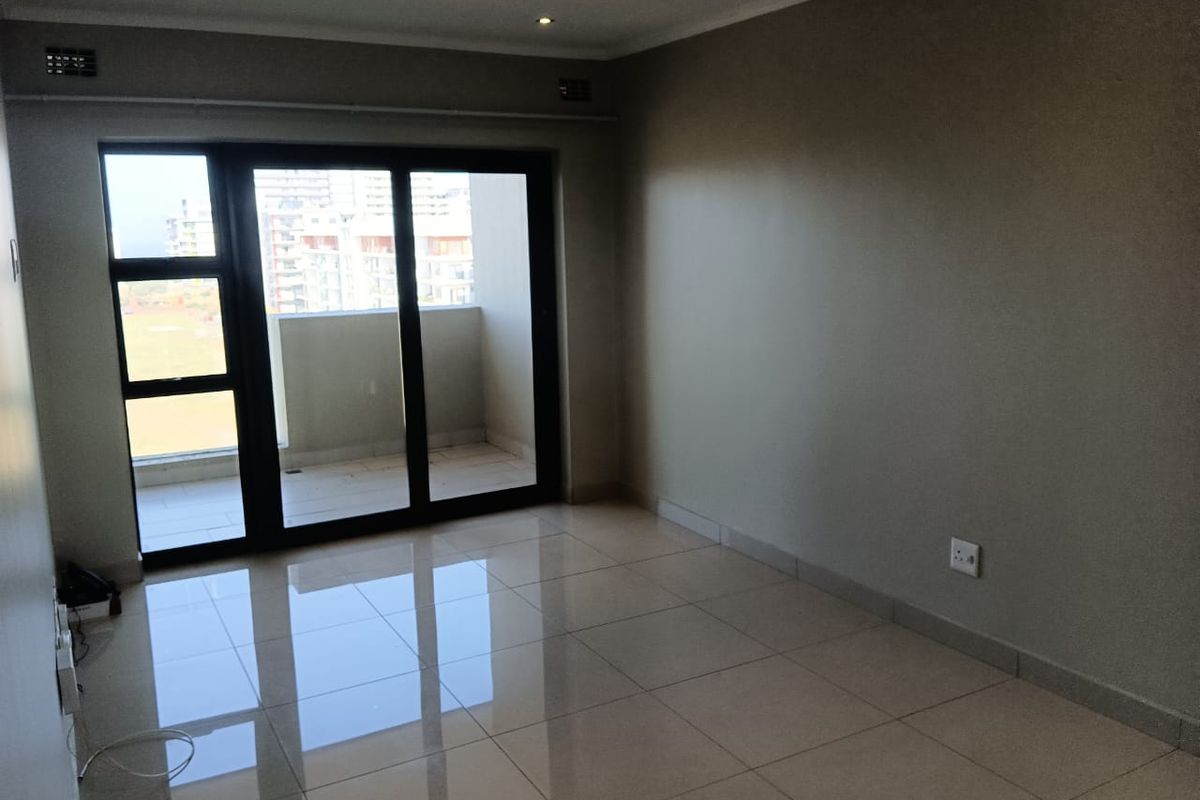 An empty, well-maintained living room featuring polished tile flooring, recessed lighting, and a large sliding glass door providing access to a private balcony.