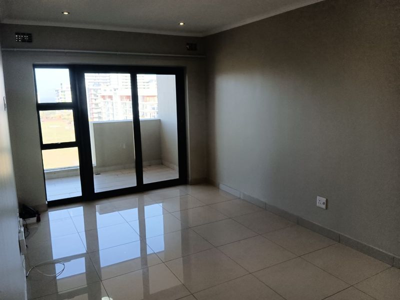 An empty, well-maintained living room featuring polished tile flooring, recessed lighting, and a large sliding glass door providing access to a private balcony.