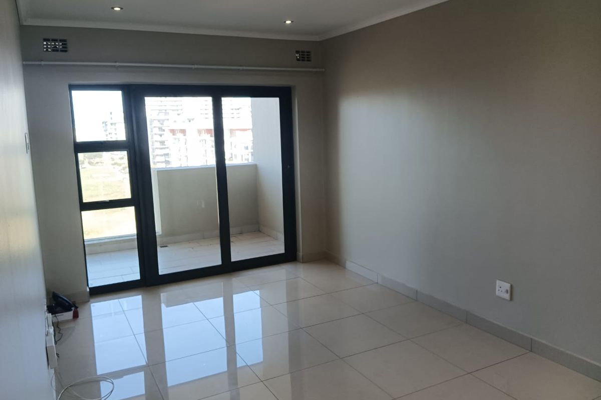 A bright, empty living room featuring neutral tiled flooring, recessed lighting, and large sliding glass doors leading to a private balcony.