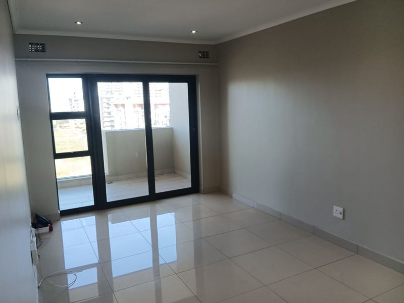 A bright, empty living room featuring neutral tiled flooring, recessed lighting, and large sliding glass doors leading to a private balcony.