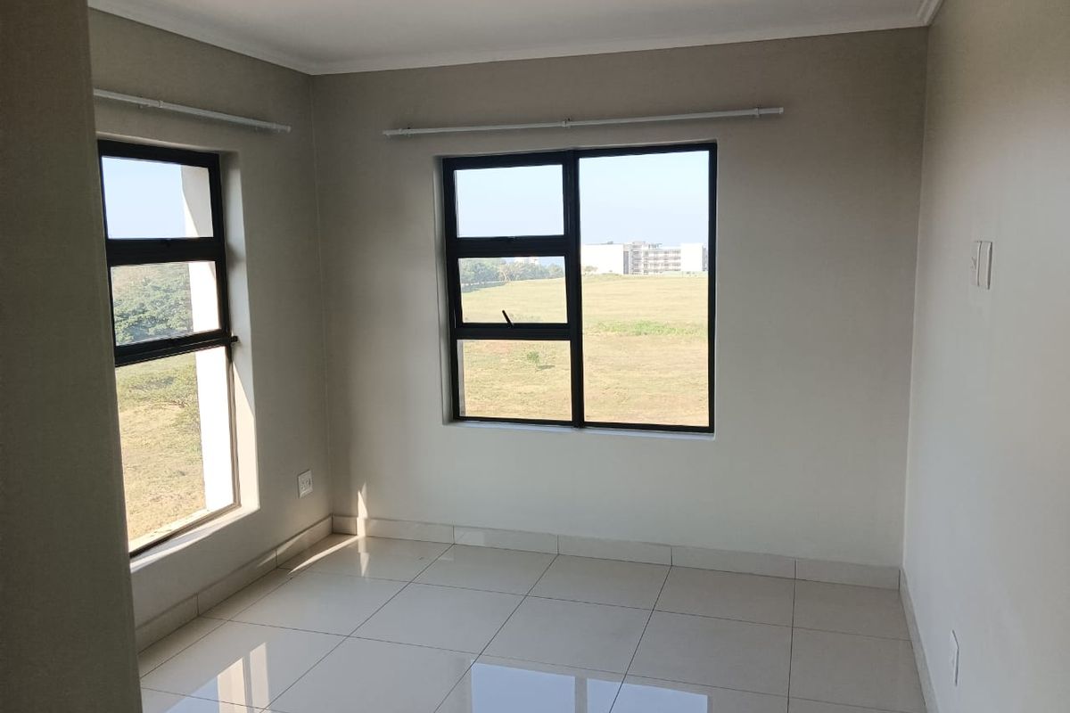 A bright, empty bedroom featuring neutral tiled flooring, modern aluminium window frames, and natural light, offering a clean canvas for personalization.