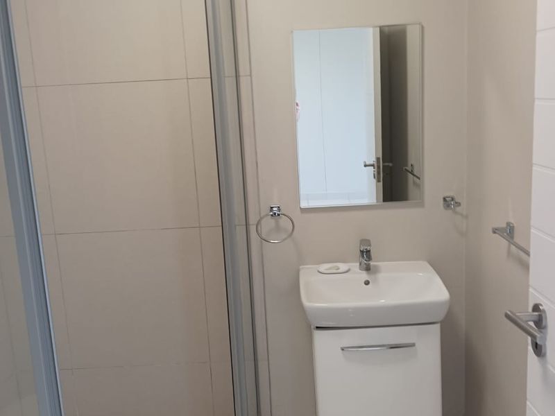 A clean, modern bathroom featuring a glass-enclosed shower, a wall-mounted vanity with a basin, and neutral tiled finishes.