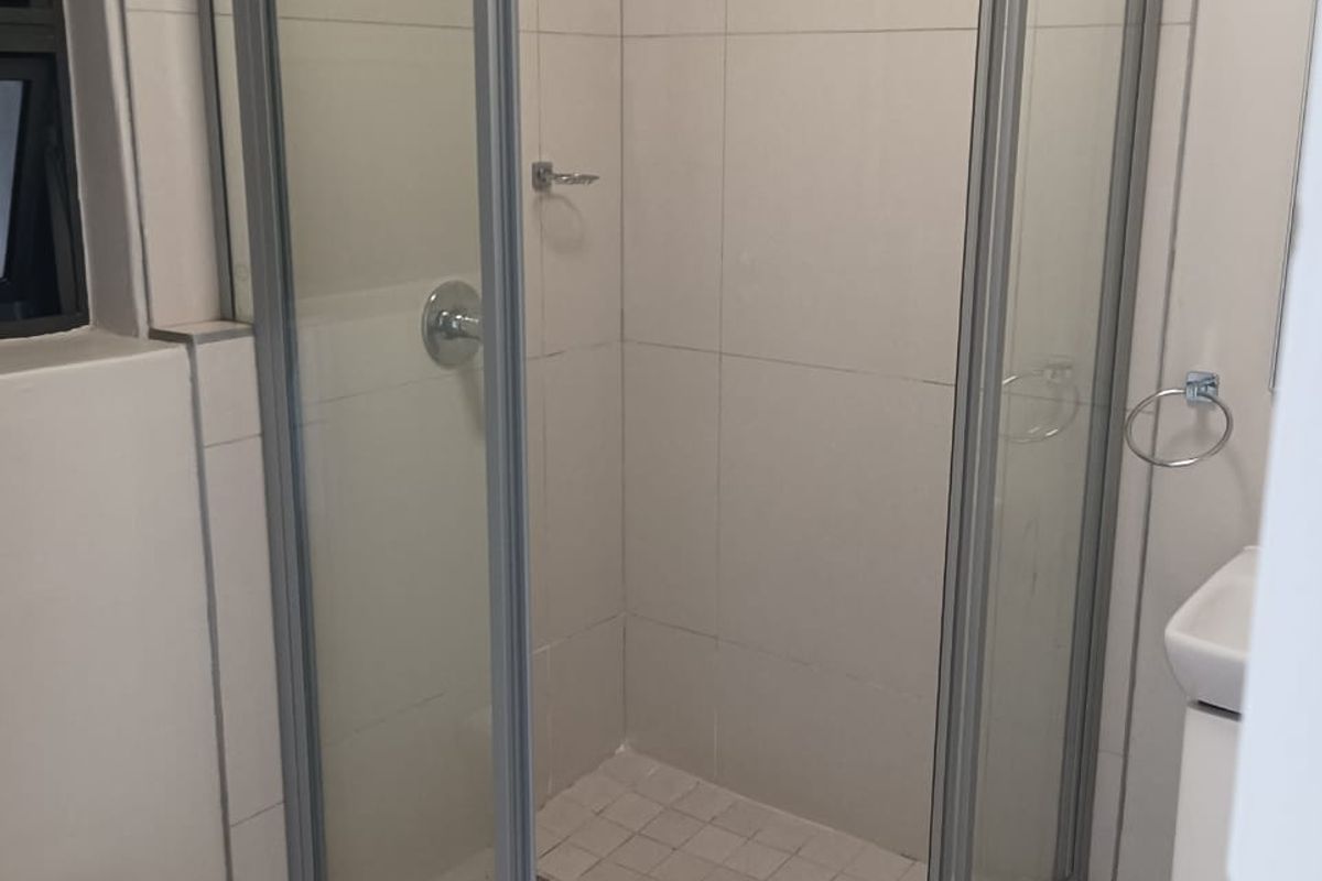 A functional bathroom featuring a corner shower enclosure, tiled walls and flooring, a wall-mounted toilet, and a vanity basin.