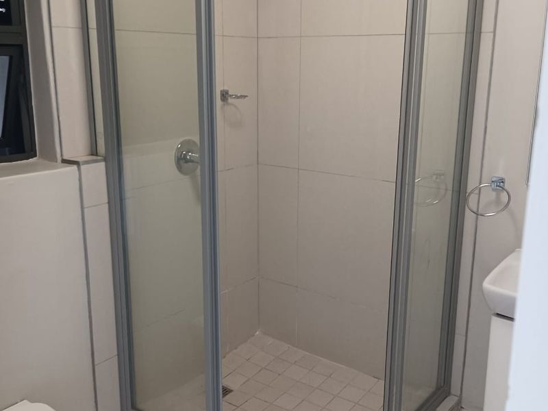 A functional bathroom featuring a corner shower enclosure, tiled walls and flooring, a wall-mounted toilet, and a vanity basin.