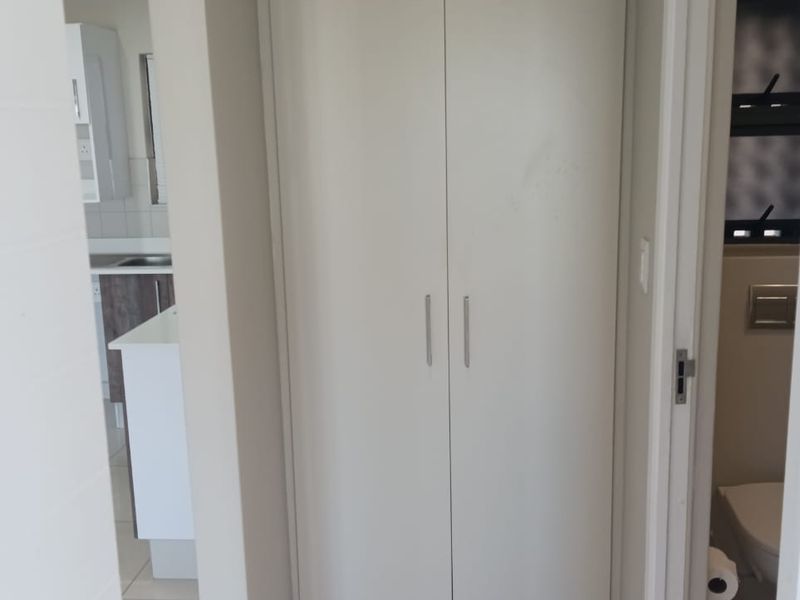 A clean hallway featuring a tall built-in storage cupboard with neutral finishes and tiled flooring, providing access to adjacent kitchen and bathroom areas.