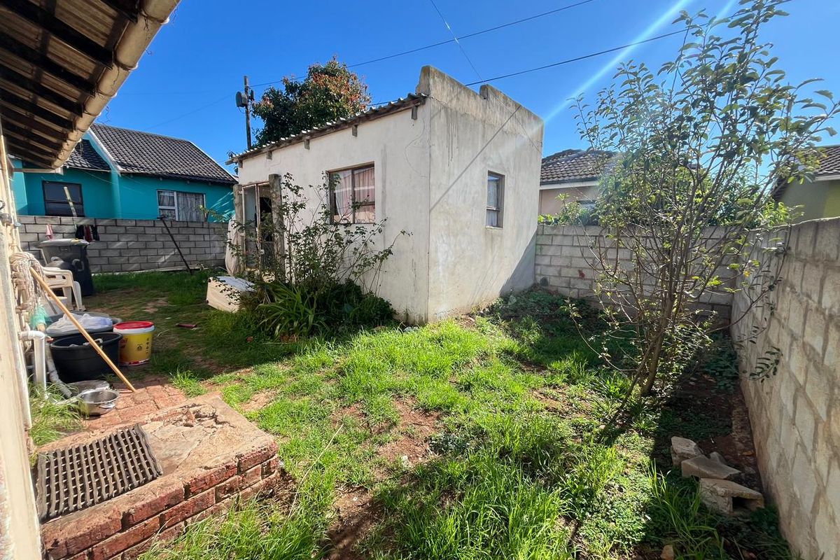 Rear yard area featuring a small outbuilding, concrete block boundary walls, and a brick drainage pit, requiring maintenance and landscaping.
