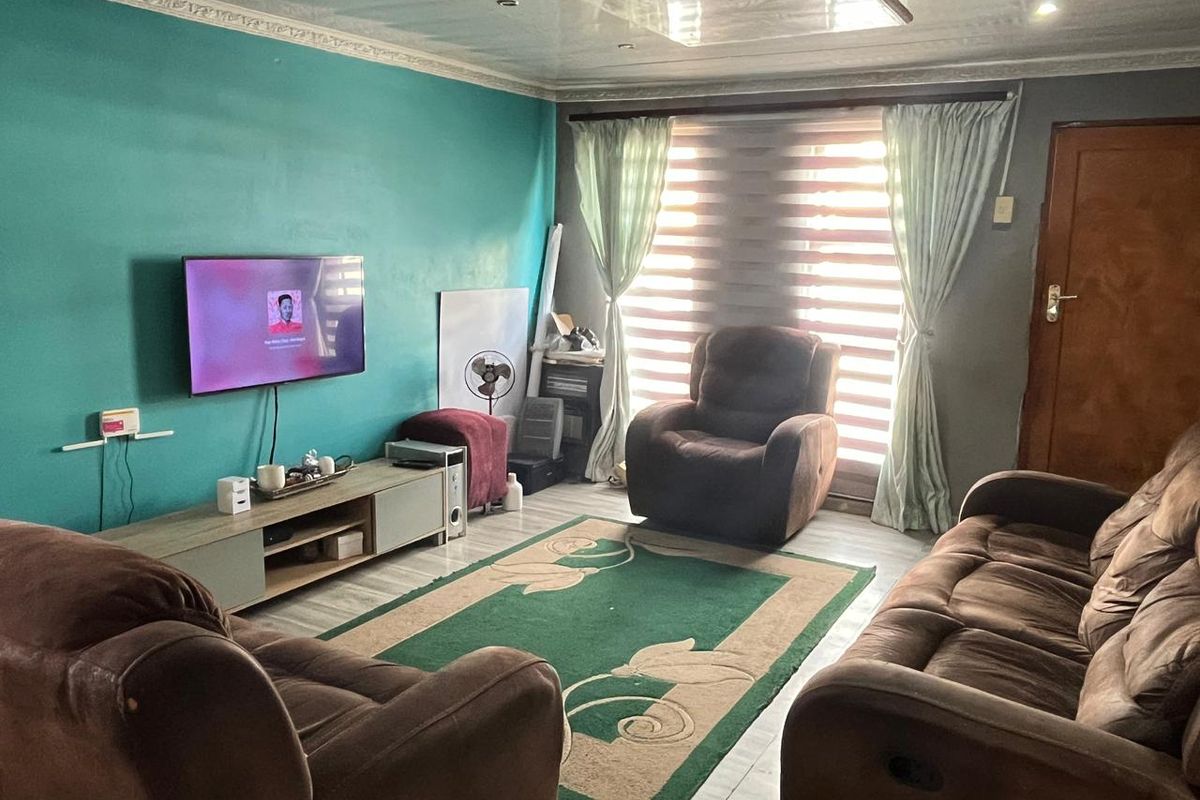 A living room featuring laminate flooring, decorative ceiling cornices, recessed lighting, and window treatments including roller blinds and curtains.