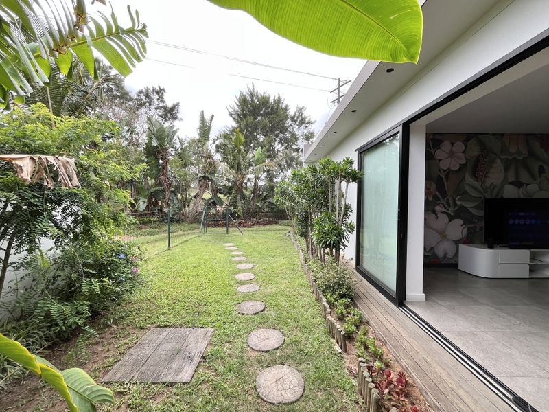 A rear garden view featuring a timber deck, sliding glass doors leading to the interior, and a landscaped lawn with a stone path.