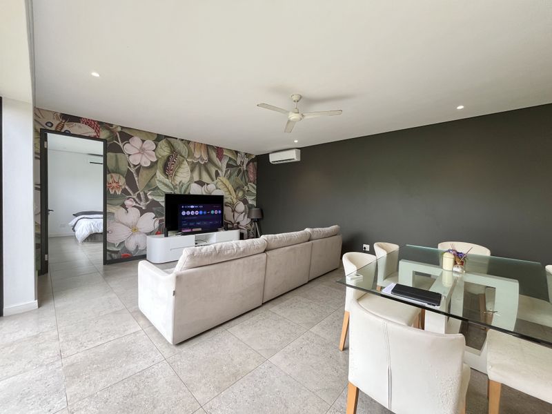 Spacious open-plan living and dining area featuring tiled flooring, a ceiling fan, split-system air conditioning, and a decorative floral feature wall.