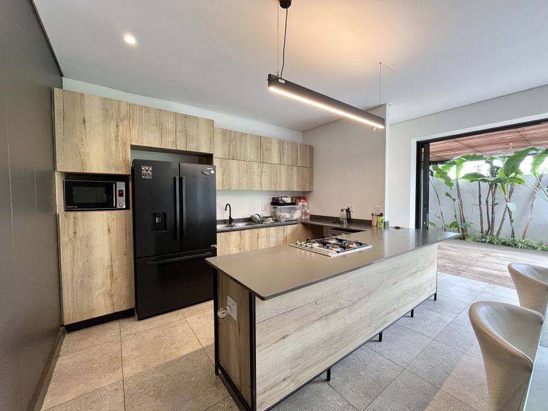 Modern kitchen featuring wood-grain cabinetry, stone countertops, a central island with a gas hob, and direct access to an outdoor patio area.