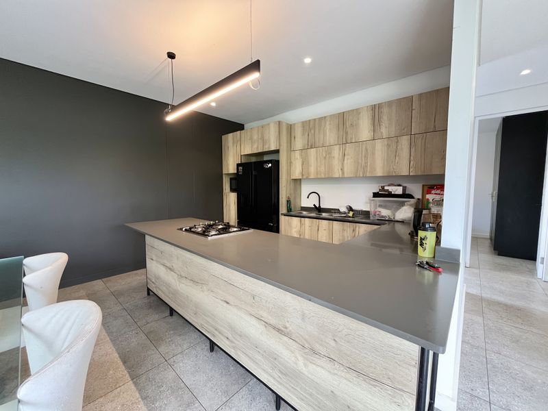 Modern kitchen featuring wood-grain cabinetry, stone countertops, a central gas hob, and sleek pendant lighting, creating a functional and contemporary cooking space.