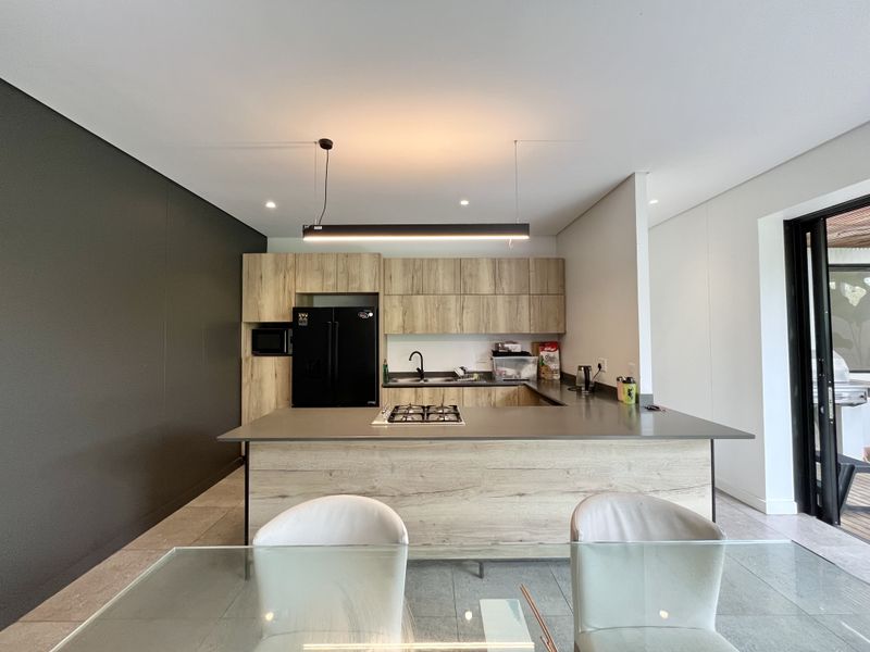 Modern kitchen featuring wood-grain cabinetry, a central island with a gas cooktop, integrated sink, and sleek pendant lighting in an open-plan layout.