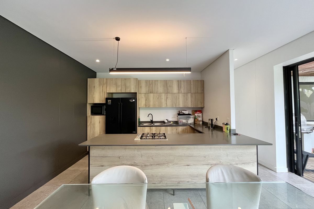Modern kitchen featuring wood-grain cabinetry, a central island with a gas cooktop, integrated sink, and sleek pendant lighting in an open-plan layout.