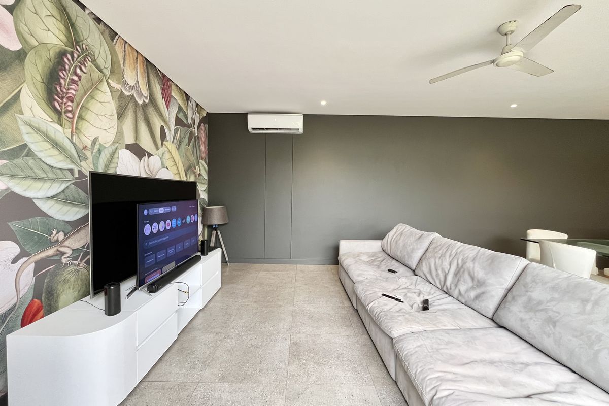 Spacious living room featuring large-format floor tiles, a ceiling fan, and a wall-mounted split system air conditioner.