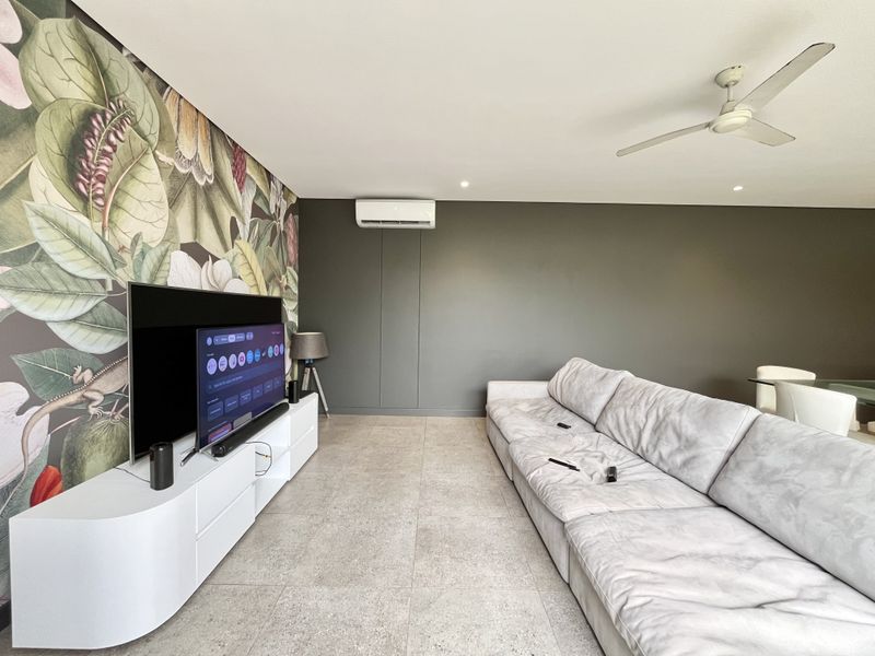 Spacious living room featuring large-format floor tiles, a ceiling fan, and a wall-mounted split system air conditioner.