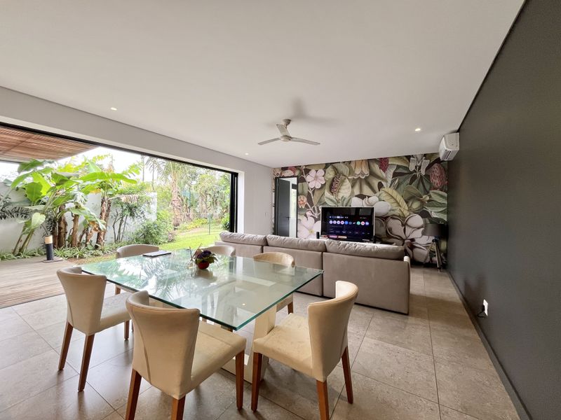 Modern open-plan living and dining area featuring large sliding doors opening to a garden, tiled floors, and a striking floral feature wall.